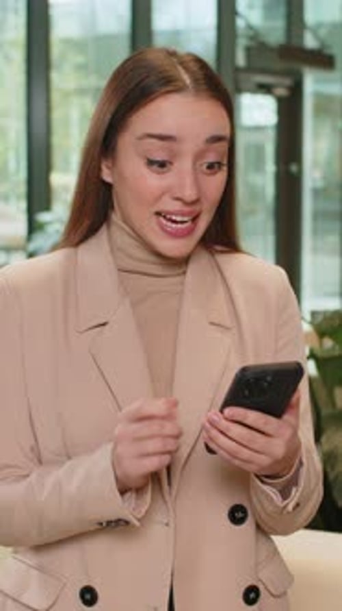 Happy Amazed Businesswoman Using Smartphone Shocked By Sudden Victory Lottery Win in Office Lobby