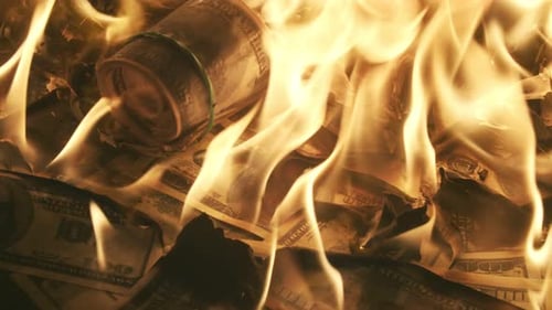 Ein Bündel von Dollars mit Gummiband, das auf einem Haufen brennender Rechnungen liegt, zerbricht und fängt auch an zu brennen