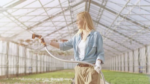 Woman Watering Flowers in Greenhouse with Hose