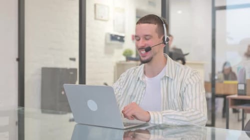 Creative Young Man with Headset Doing Video Chat on Laptop in Call Center