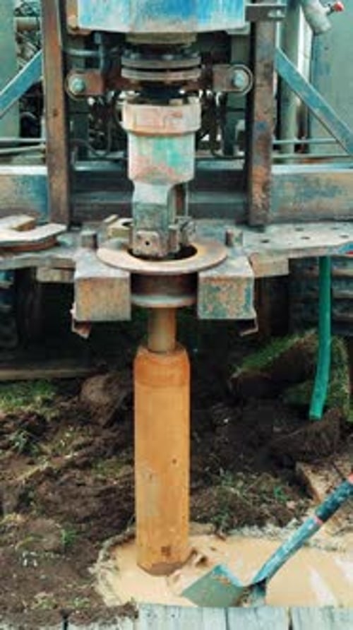 Large forcer is rotating in the muddy puddle in the ground. A shovel is helping the work of machine.