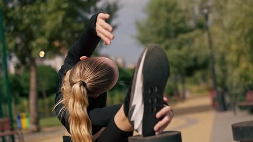 Close-up A young girl sports trainer stretches her lateral back muscles by throwing her leg on high