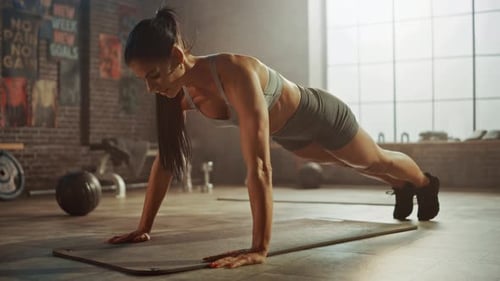 Strong and Fit Athletic Woman in Sport Top and Shorts is Doing Push Up Exercises in a Loft Style In