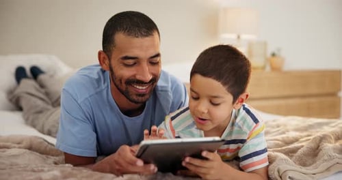 Father and Son Use Tablet on Bed