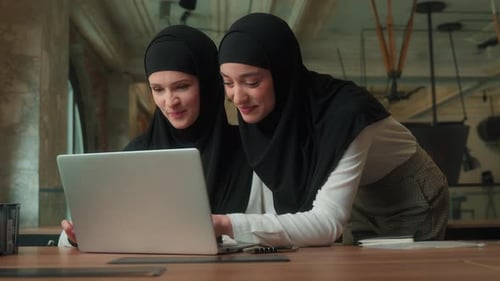 Two Women in Hijabs Work Together on Laptop