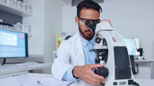 Männlicher Wissenschaftler betrachtet mit Mikroskop eine Blutprobe und schreibt Notizen zu seinen Ergebnissen