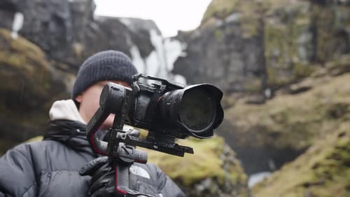 Young adult holds a camera with a stabilizer outdoors