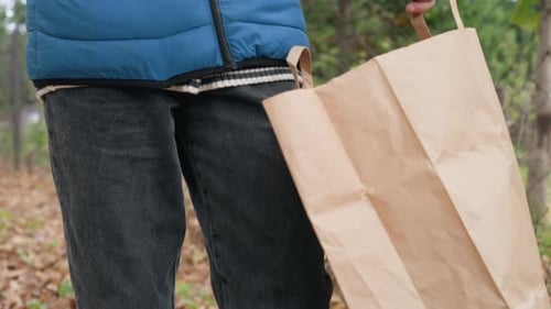 Un niño sostiene una bolsa de papel marrón con una hoja de otoño que gira en sentido horario y antihorario al aire libre