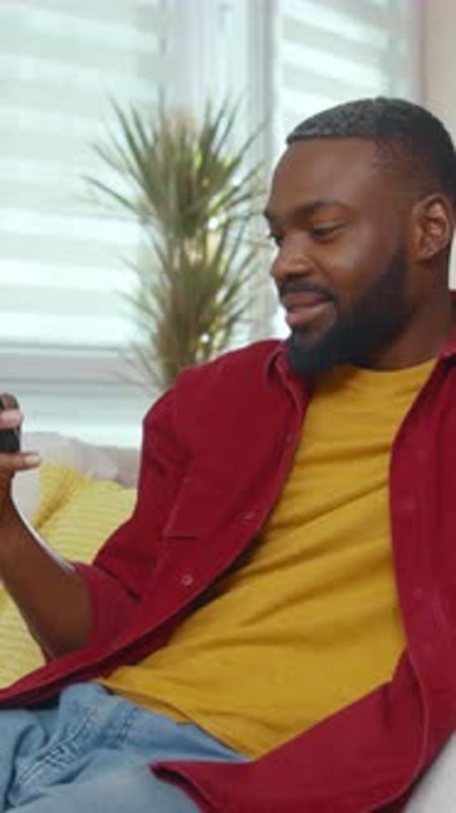 Man Smiles While Looking at Phone on Sofa