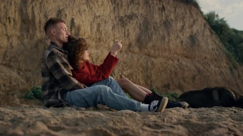 Happy Man and Woman Relaxing on Sandy Beach. Cheerful Girl Taking Photo