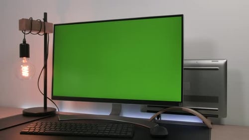 Modern monitor with green screen display standing in a desk of an office with a laptop and a lamp bu