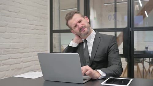 Man Massaging Neck While Working at Laptop