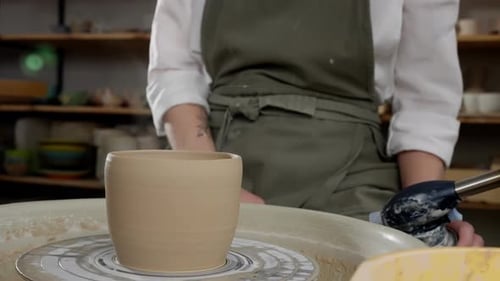 A Woman is Sitting at a Pottery Wheel Creating a Clay Cup