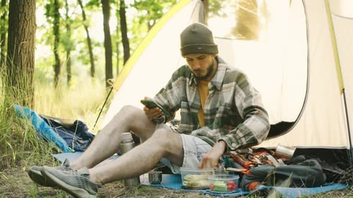 Man Using Phone While Camping, Eating Lunch