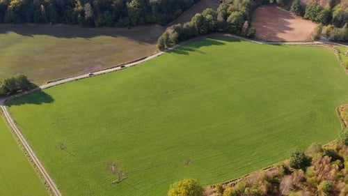 Aerial view over green field and cars driving along country roads