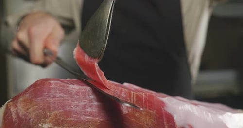 Close up macro of a chef who cuts a slice of ham, of excellent quality, with the knife according t