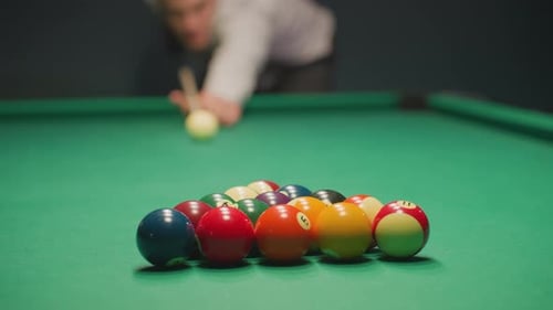 Blurred Player Focusing on Pool Shot Over Green Table in Dimly Lit Game Room