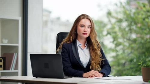 Look Into Camera in a Modern Office with a Large Window a Beautiful Worker in a Blue Shirt with a