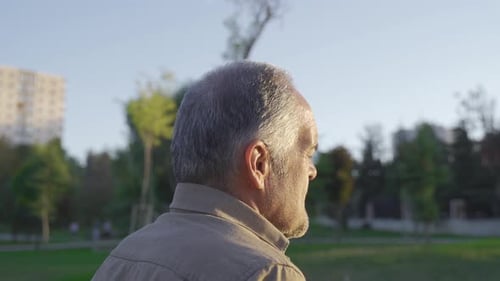 The old man is walking outdoors.