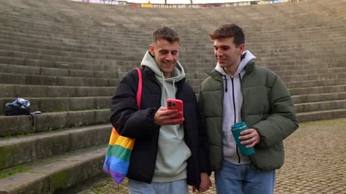 Young gay couple holding hands and looking at smartphone