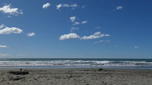 Clouds appear almost motionless as small waves roll into sandy beach on a beautiful summer's day - S