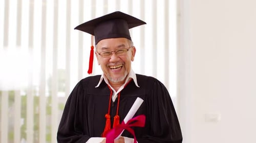 Asian elderly in cap and gown smile and celebration proud success graduate. Cheerful senior man hold