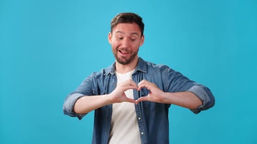 Man Makes Heart Shape Gestures on Blue Background
