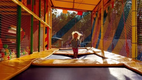 Cheerful Little Preschool Girl Jumping on Trampoline in Children Amusement Park