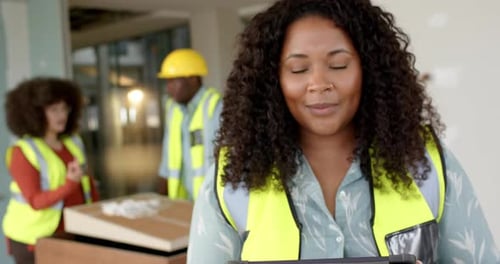 Smiling casual biracial female architect with tablet in office, slow motion, copy space