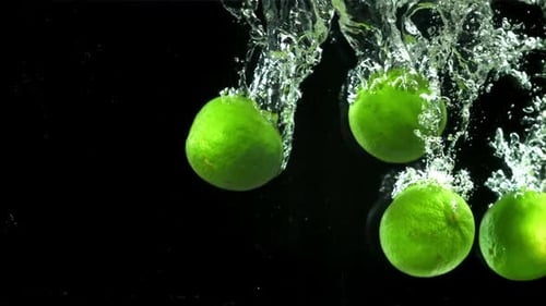 Limes Splashing in Water on Black Background