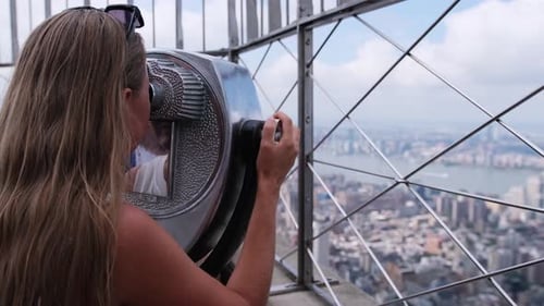 Visitante apreciando a vista panorâmica com binóculos do arranha-céu de Nova York