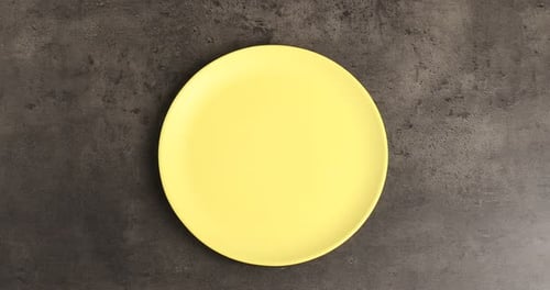 Hombre poniendo el plato y los cubiertos sobre una mesa gris, vista desde arriba