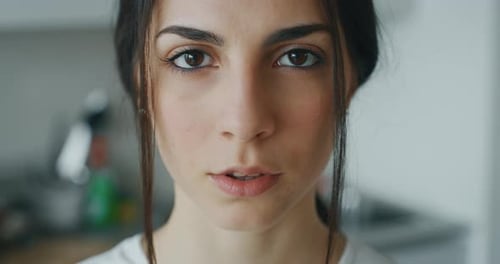 Slow motion close up of an young woman is looking and smiling in the camera in the kitchen.