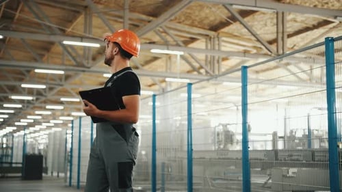 Manager in orange hard hat stands in the factory and looks around
