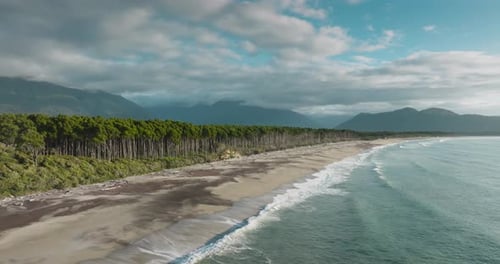 Panoramic aerial view of long, wild and rugged sandy coastline covered in driftwood with windswept n
