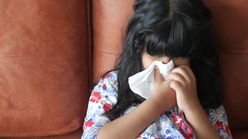 Child Wipes Face with Tissue on Brown Couch