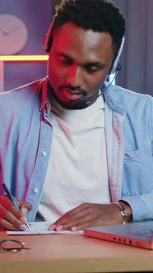 Smiling Man with Headset Writing at Desk