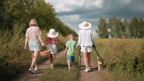 Rear View of Family Walking on Dirt Road with Dog Going for Picnic in Countryside