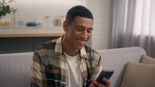 Smiling Young Man Using Mobile Phone on Sofa