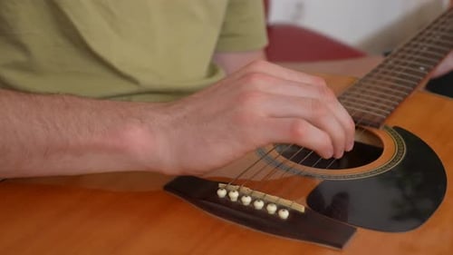 Adult Man Guitarist Sitting in the Room Playing Acoustic Guitar Fingering Strings Chords Close Up