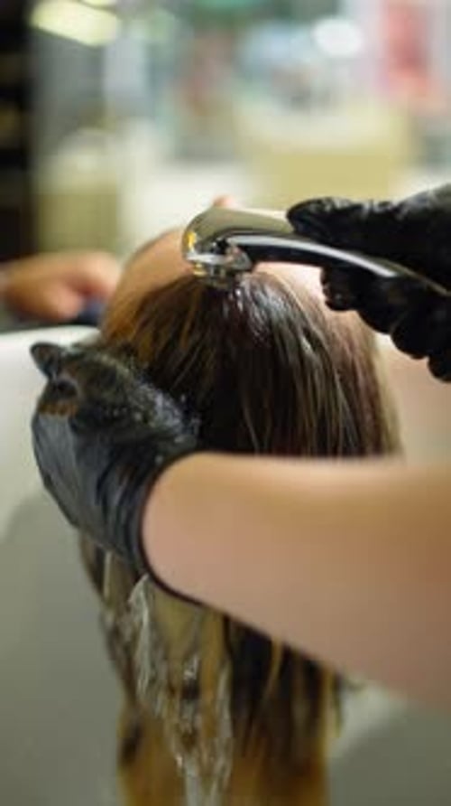 Hairdresser Rinsing Blonde Highlights in Salon Sink