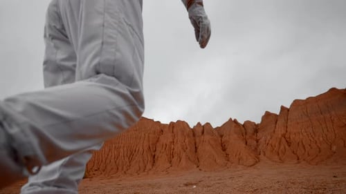 Unrecognisable Astronaut in Costume and Helmet Walking on Mars Orange Surface