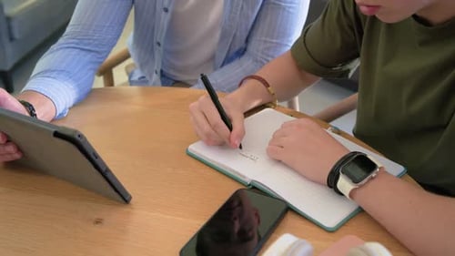 Das Tablet wird zum Nachhilfeunterricht zum Notizbuch geneigt, mit der linken Hand zeigt und mit der rechten Hand Notizen schreibt