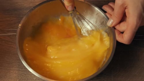 Schaumige gelbe Mischung in einer Edelstahlschüssel, Küchenszene, bei der Eier in einer Schüssel energisch verquirlen werden