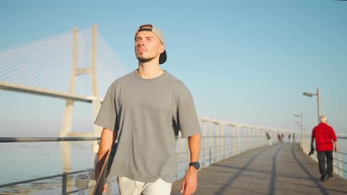 Young Man Walking on Pier with Skateboard