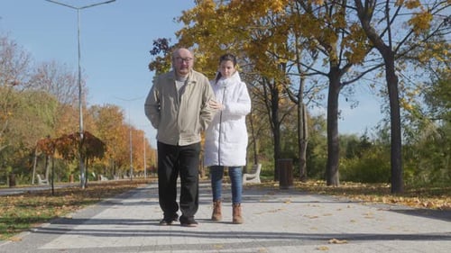 Elderly Man and Young Assistant Strolling Together in Autumn Park