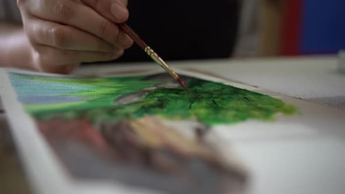 wide angle close up shot of an artist's hand as she creates a mountain landscape painting using goua