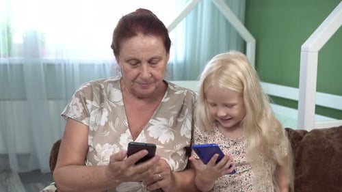 Grandmother and Child Granddaughter Use Smartphones