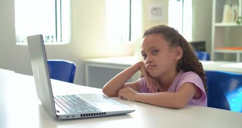 African girl child in purple shirt sitting at school facing laptop, camera moving, appearing bored