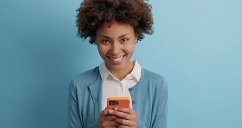 Smiling Young Woman Using Smartphone on Blue Background